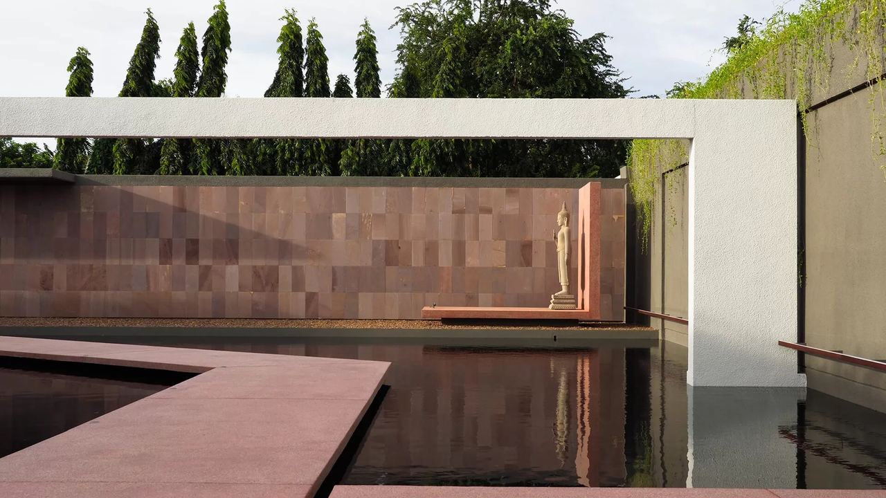 A still pool and a carved figure against a terracotta wall in a courtyard at The Balé Phnom Penh